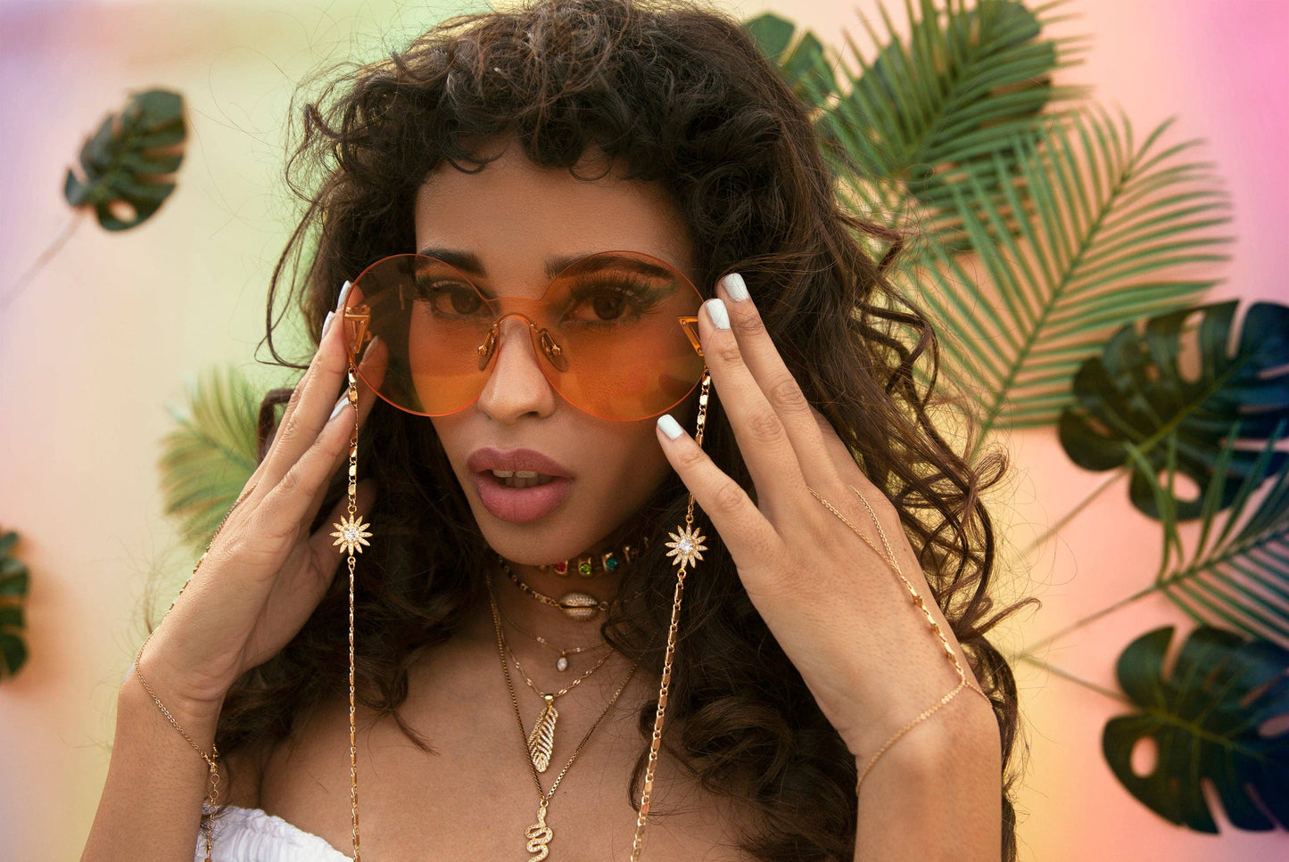 Woman wearing orange sunglasses with a tropical leaf background