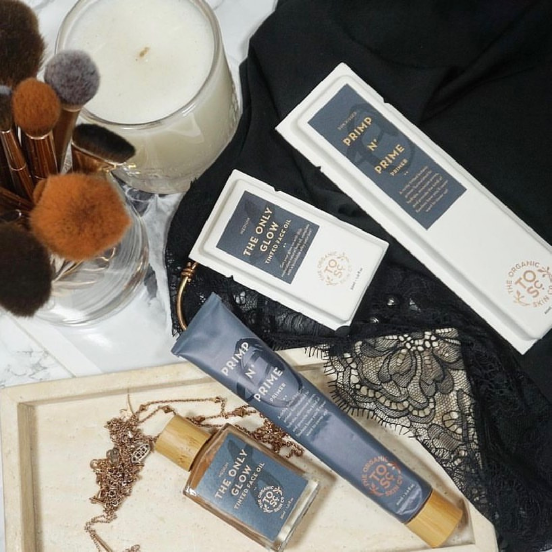 Cosmetic products including a candle, brushes, and skincare items on a textured surface.