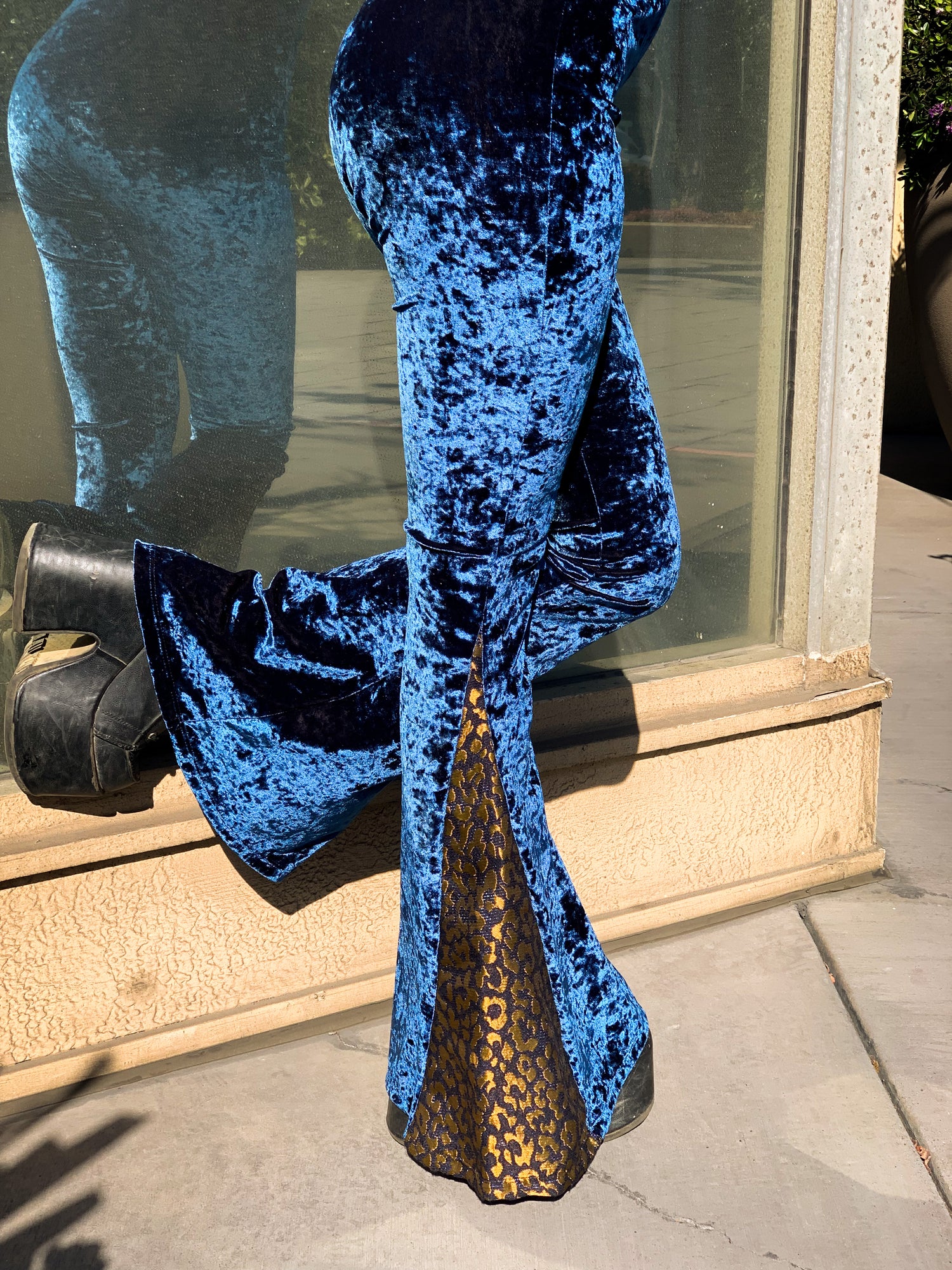 Royal blue velvet high waist flare pants on a woman standing in front of a window