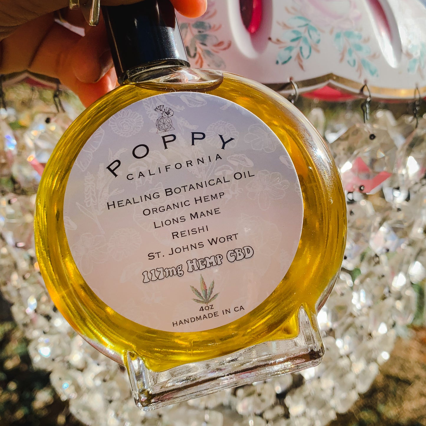 healing botanical oil bottle being held in front of a vintage lampshade