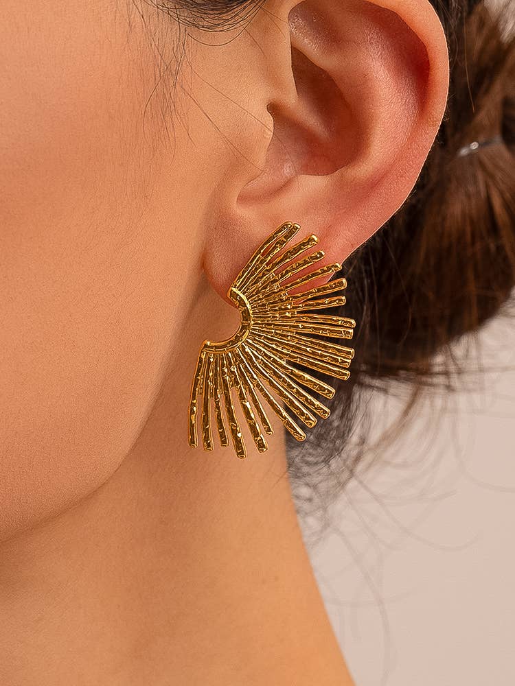 Gold sunburst earrings in a womans ear