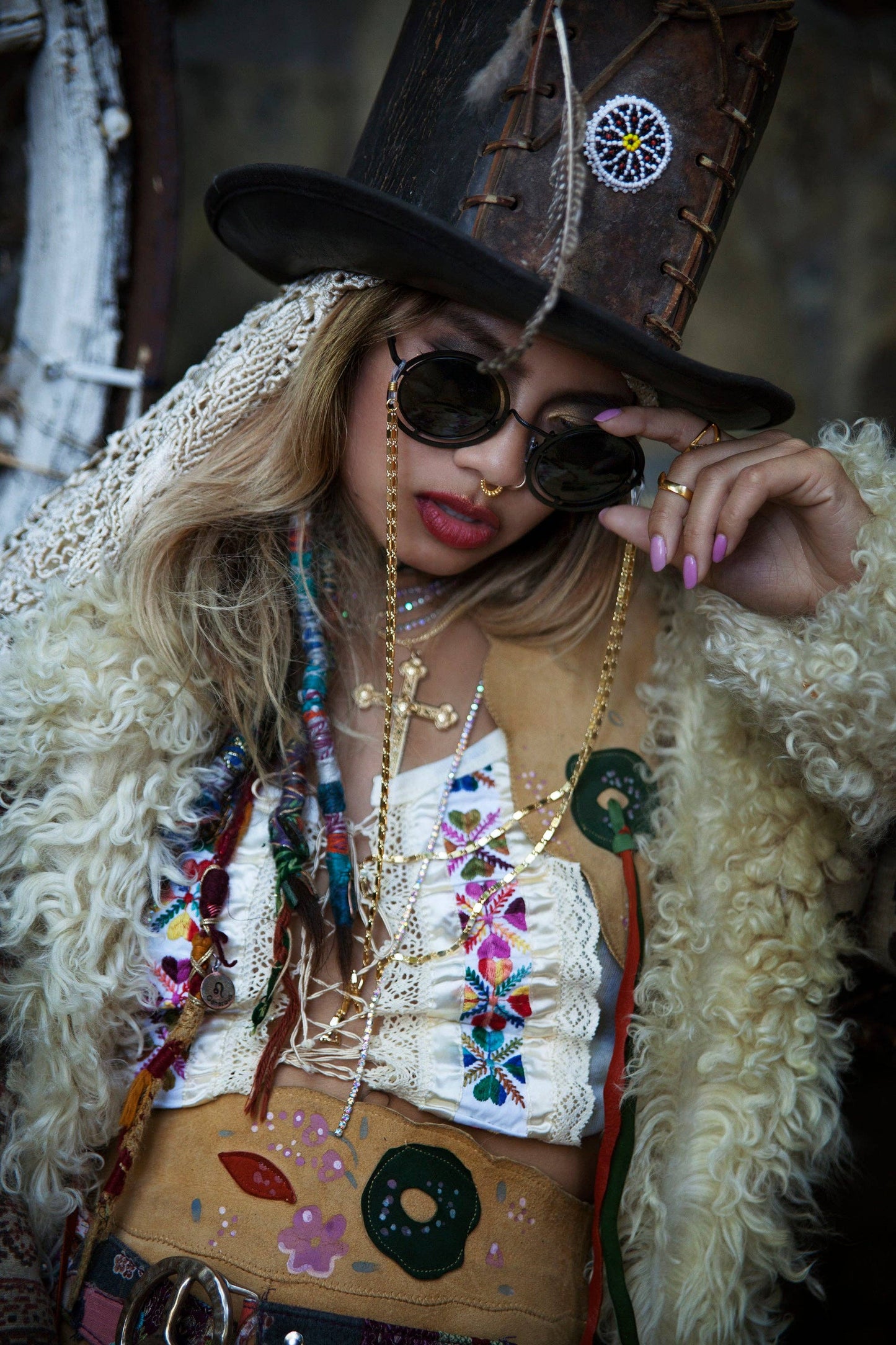 Person wearing a decorative outfit with sunglasses and a hat, holding a colorful bag.