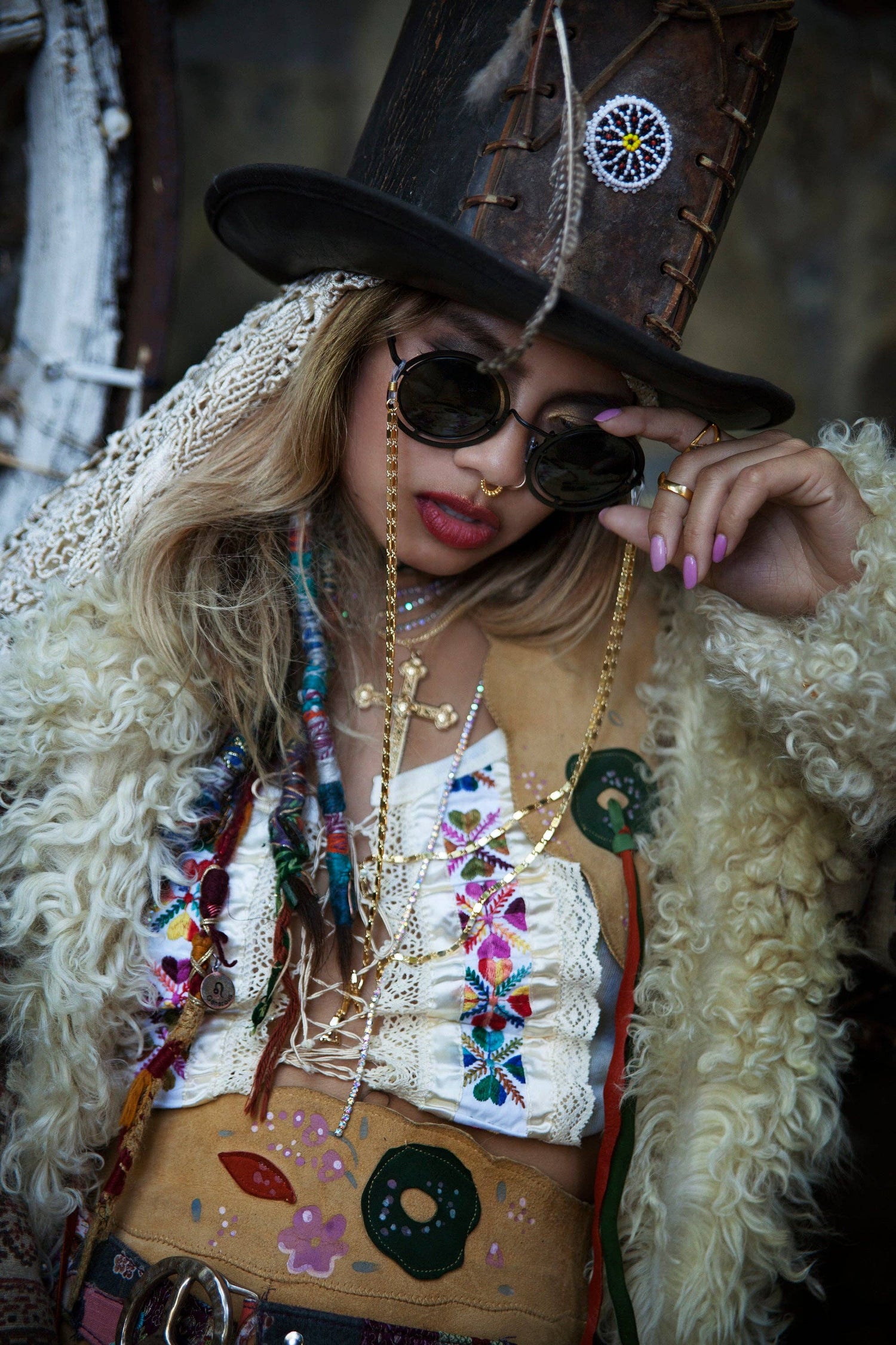 Person wearing a decorative outfit with sunglasses and a hat, holding a colorful bag.