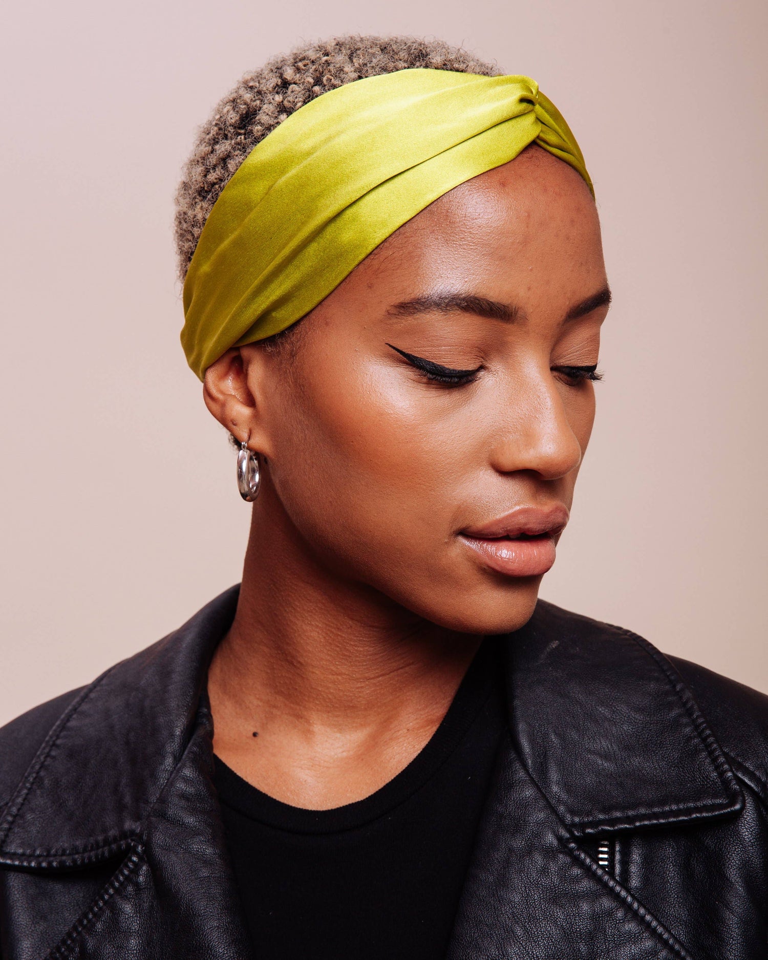 Woman wearing a bright green headscarf against a beige background