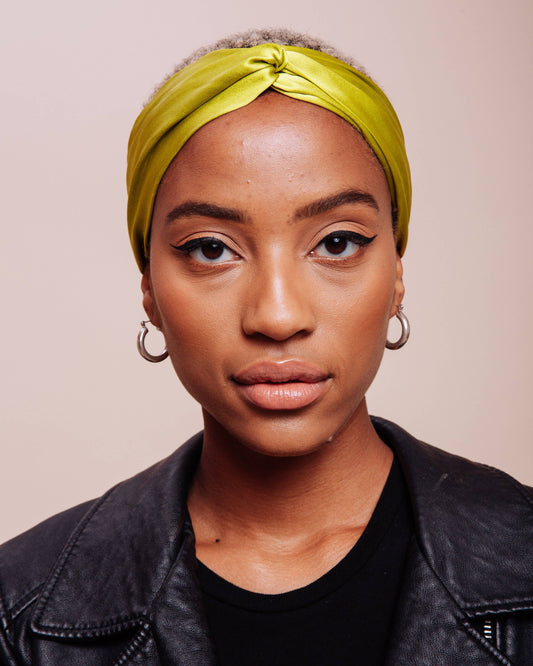 Woman wearing a yellow headscarf and black leather jacket against a beige background