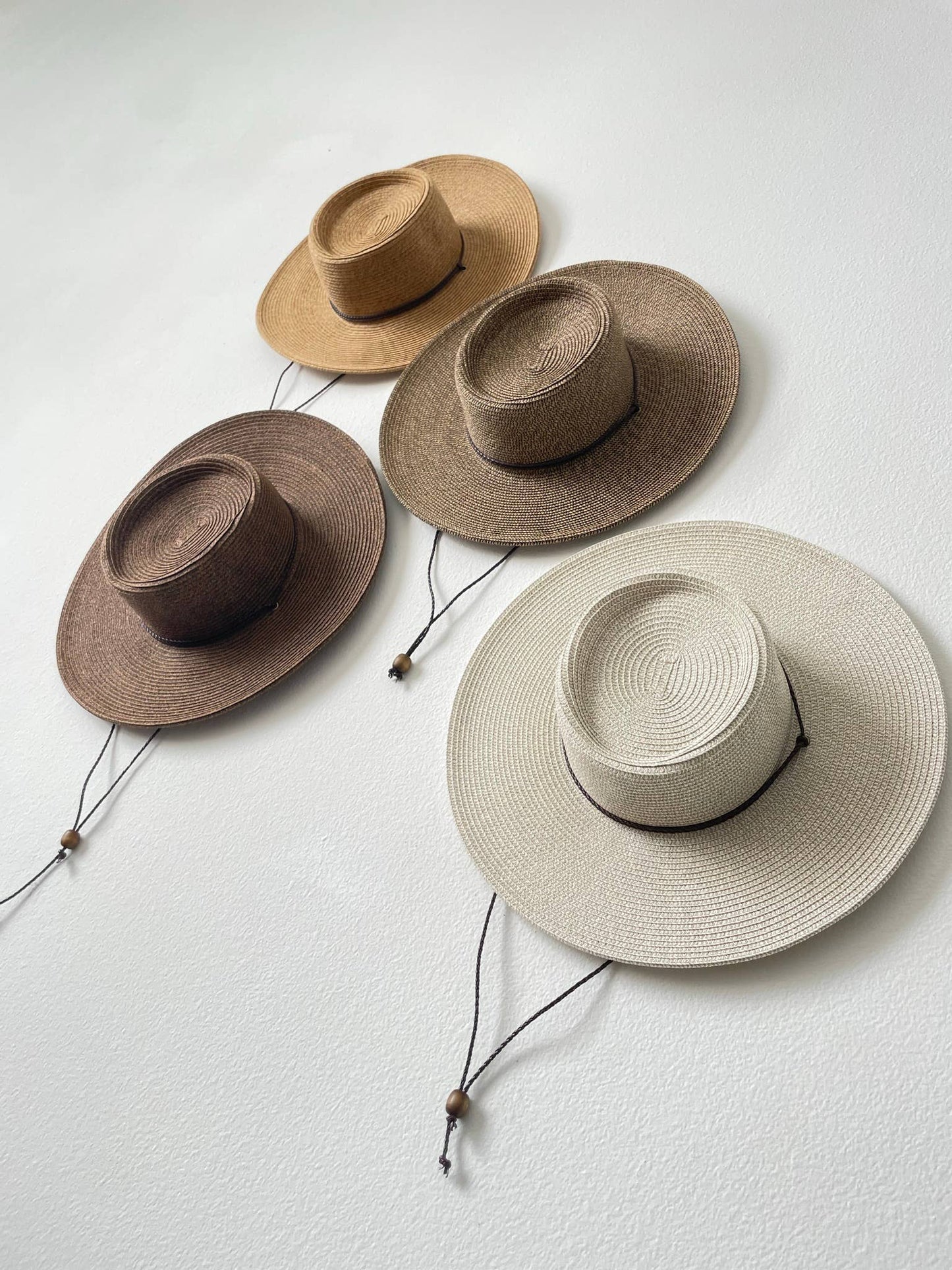 Four straw hats in different colors on a light gray background