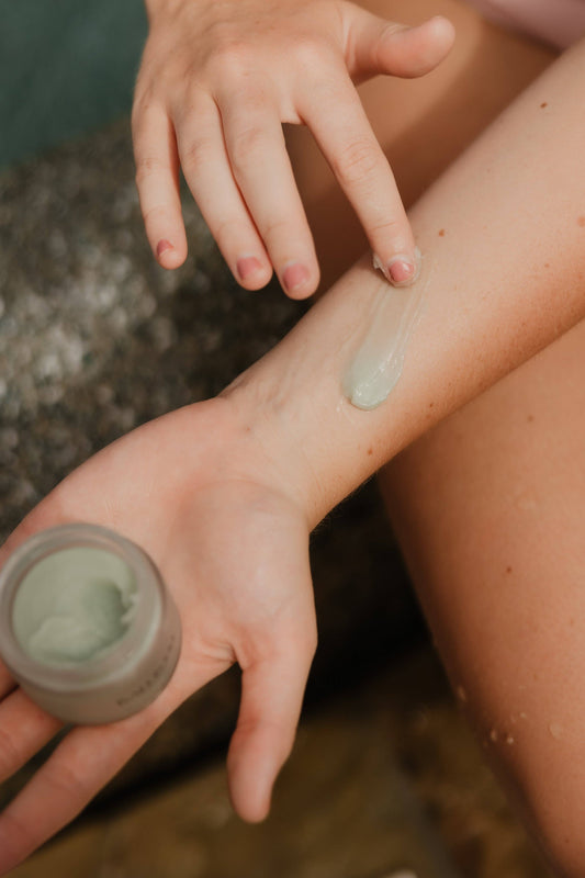Hand applying cream to another hand with a jar of cream in the background