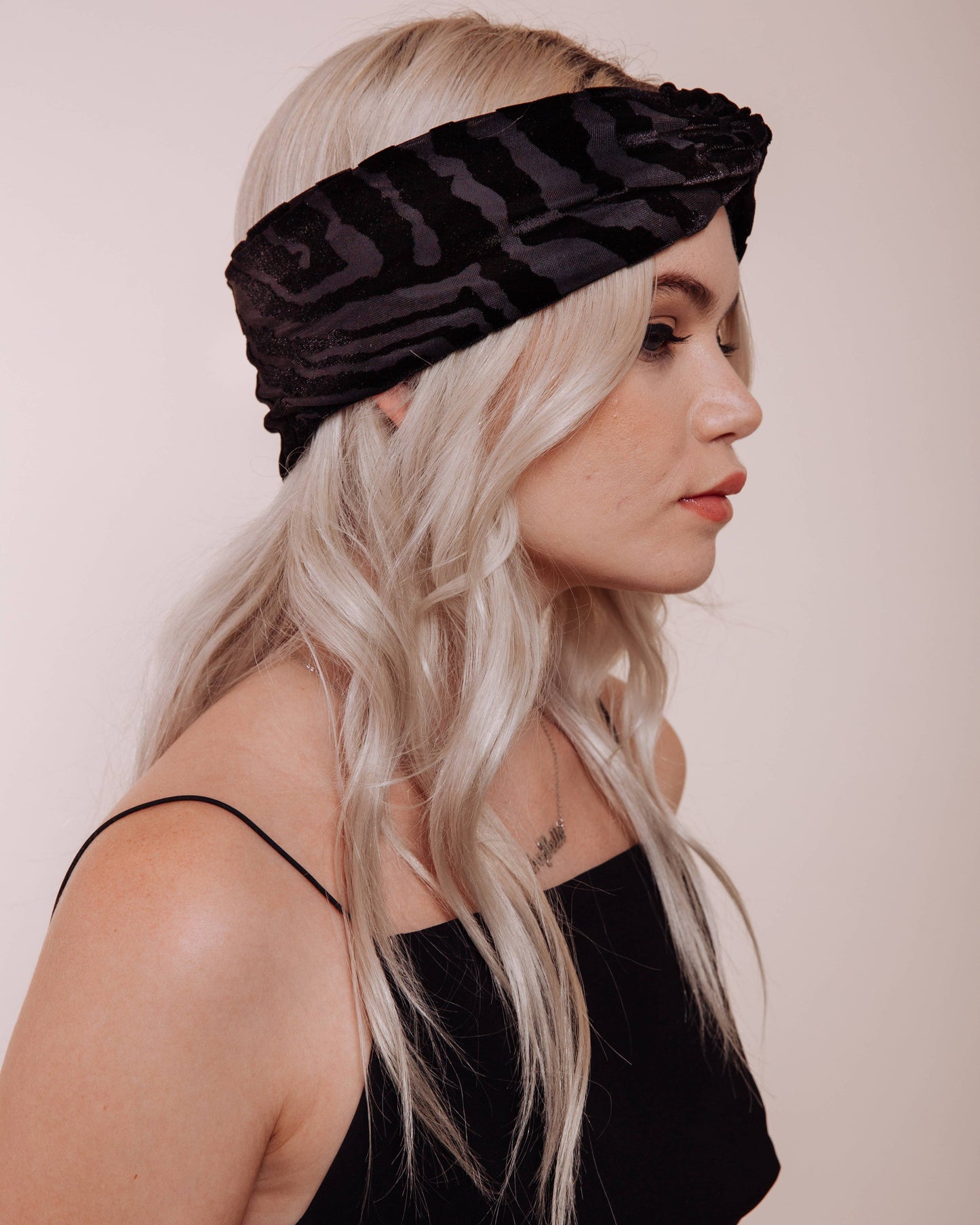 Woman wearing a black headband with a textured pattern against a plain background