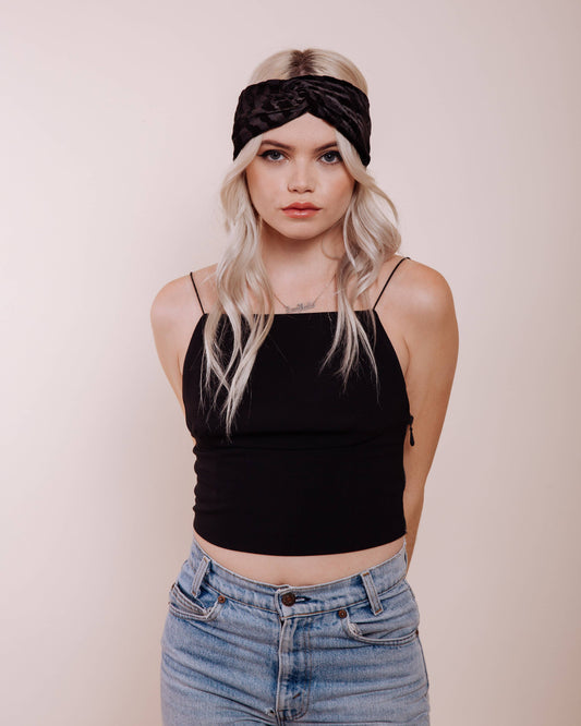 Woman wearing a black headband, black top, and blue jeans against a plain background