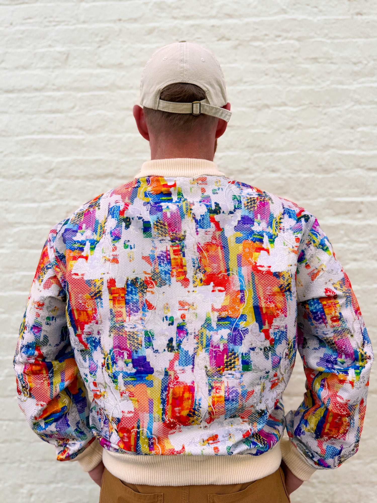 Person wearing a colorful jacket with a white brick wall background