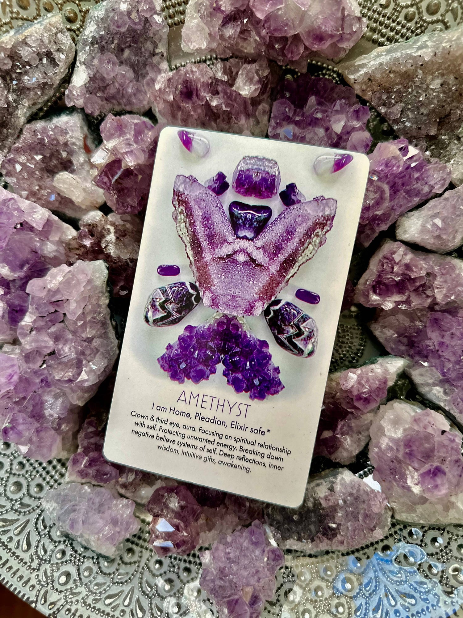 Amethyst crystal card surrounded by amethyst crystals on a decorative surface