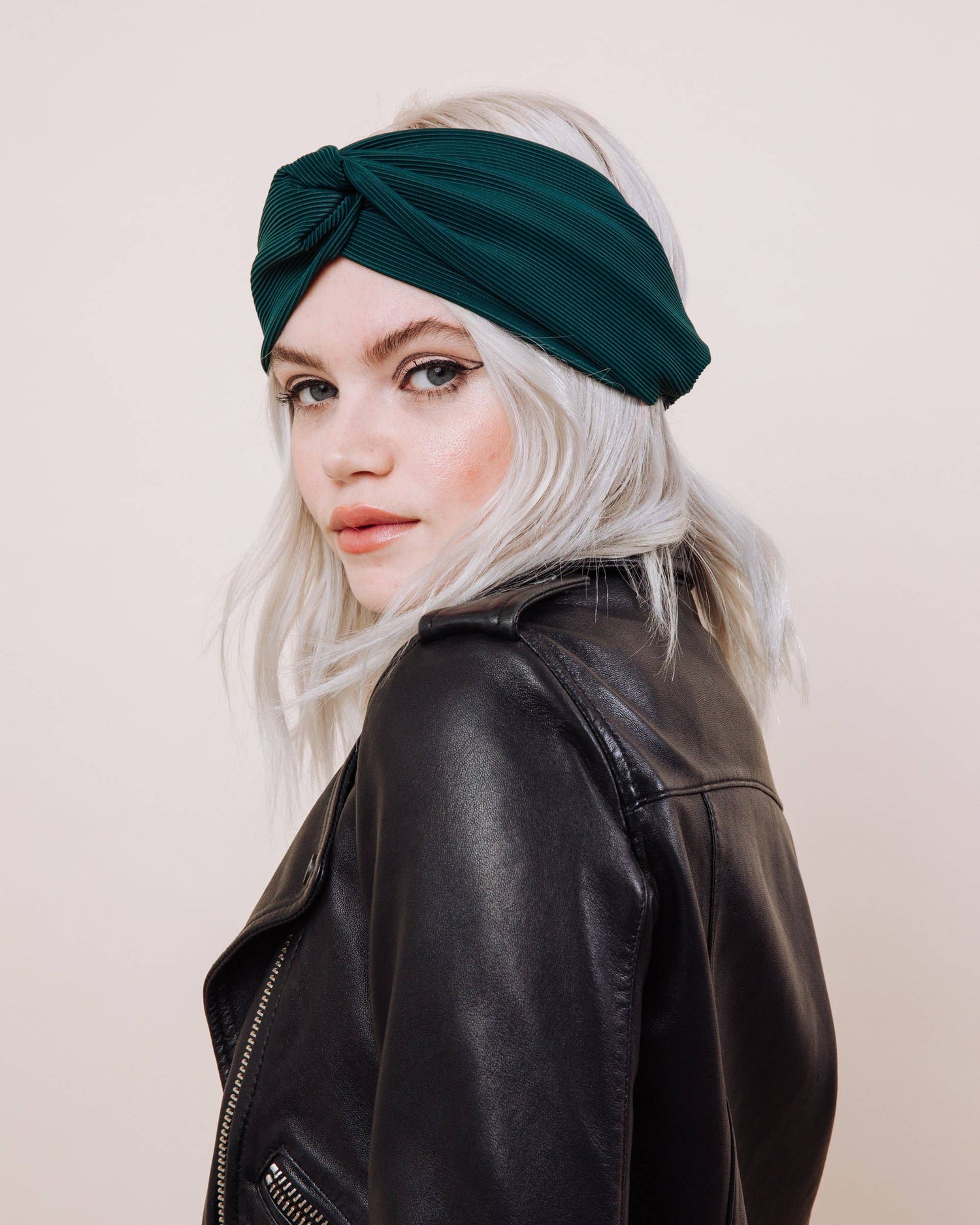 Woman wearing a green headband and black leather jacket against a plain background