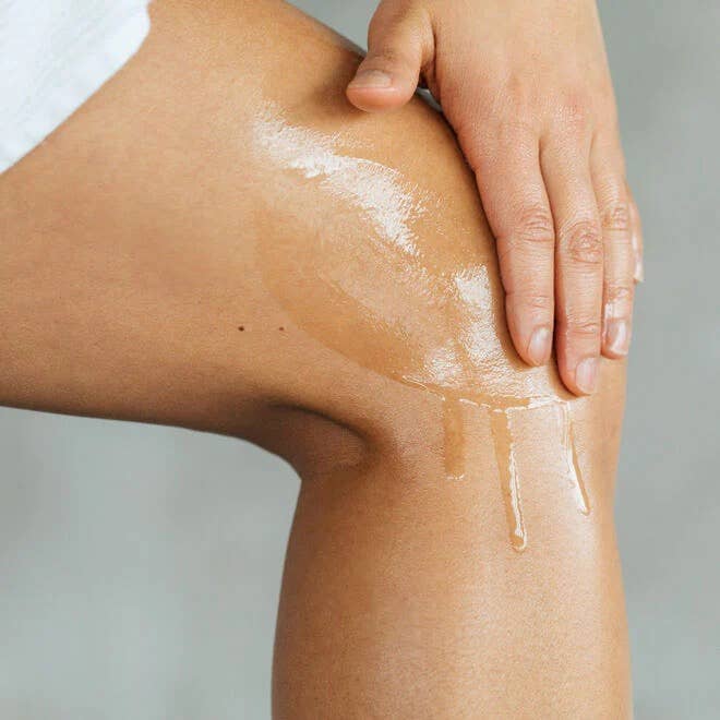 Person applying a white cream or lotion to their leg with a neutral background
