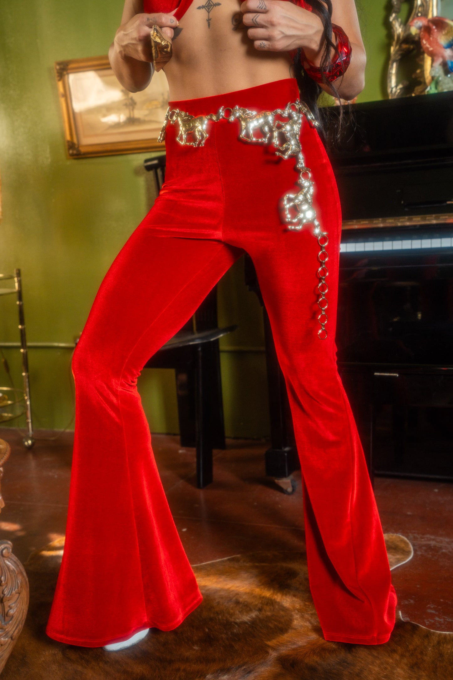 Person wearing red bell-bottom pants with decorative elements in a room with a piano and green wall.