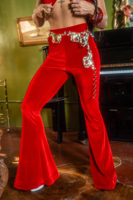 Person wearing red bell-bottom pants with decorative elements in a room with a piano and green wall.