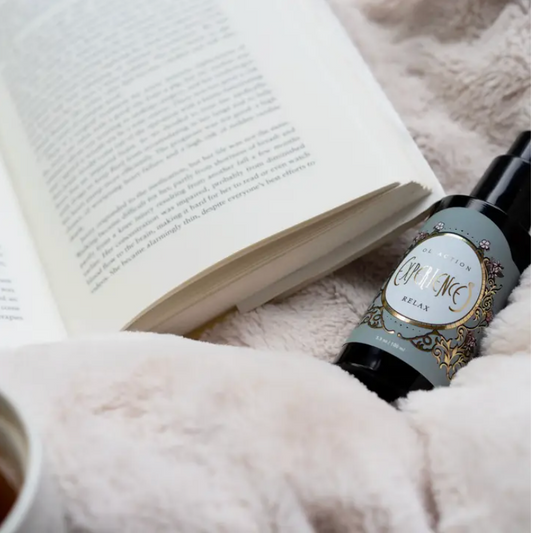 A relaxing aromatherapy mood spray next to a book and fluffy blanket to evoke a sense of coziness