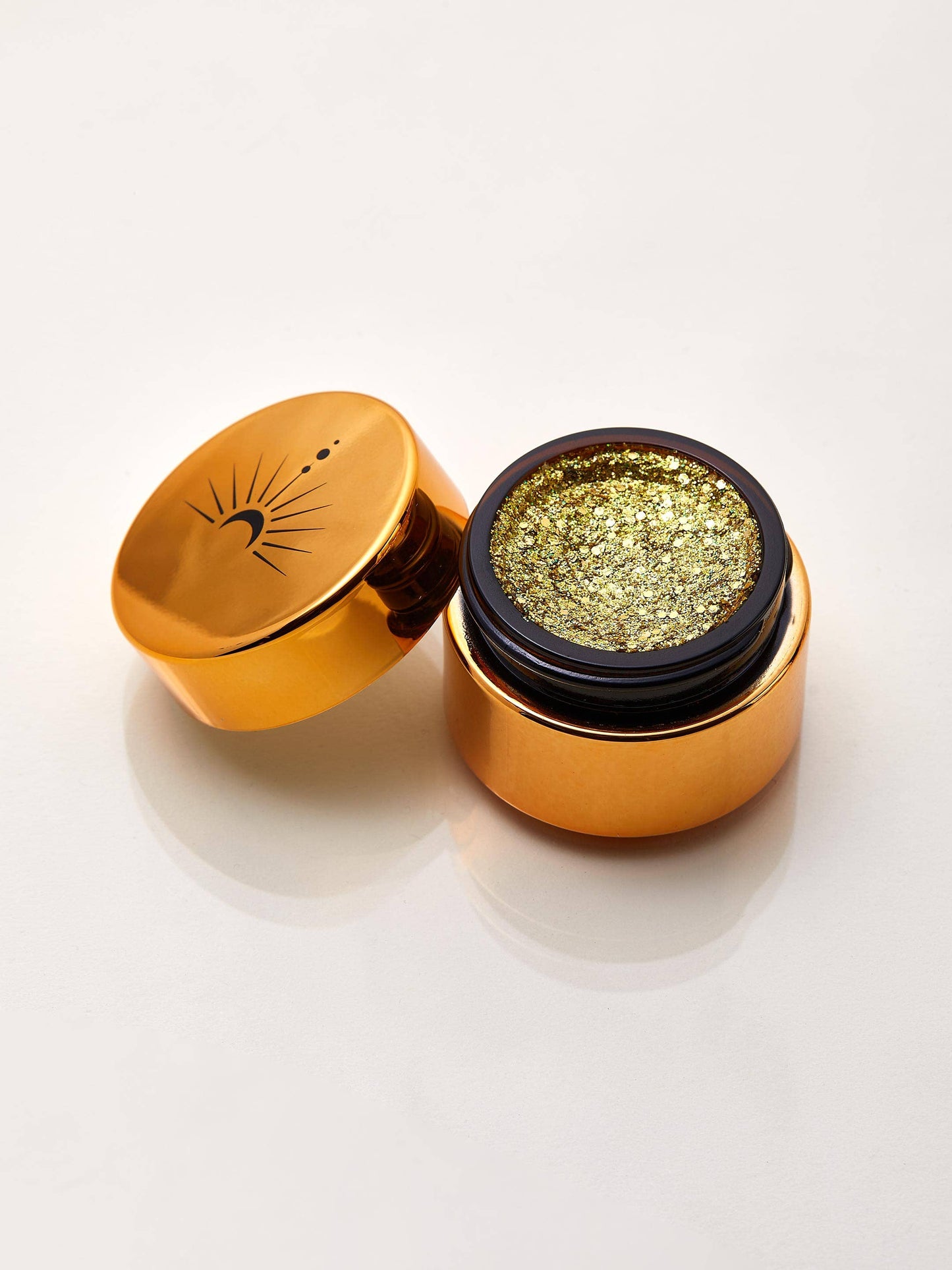 Gold container with a lid open, revealing gold glitter on a white background