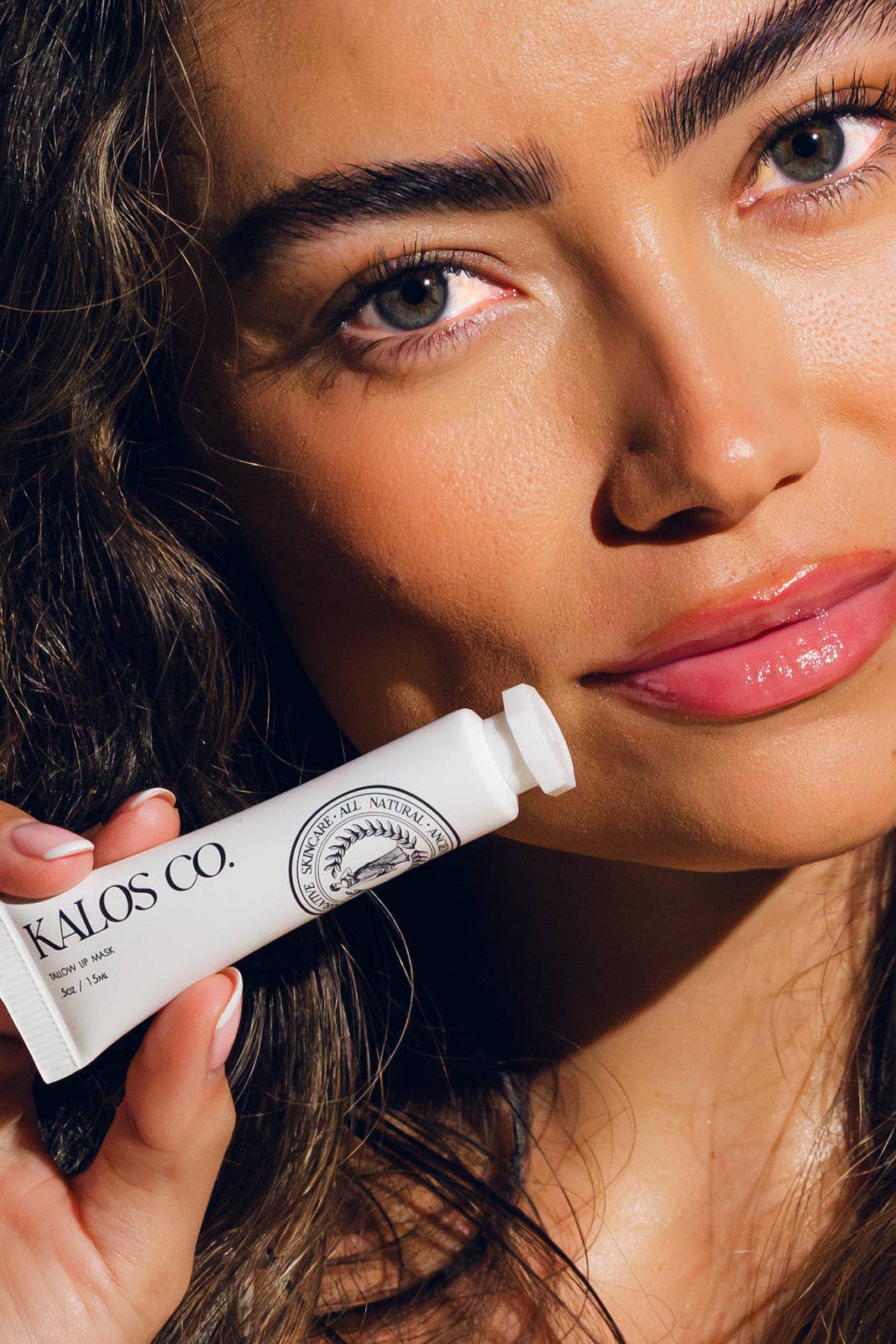 Woman holding a tube of Kallos Co. product close to her face