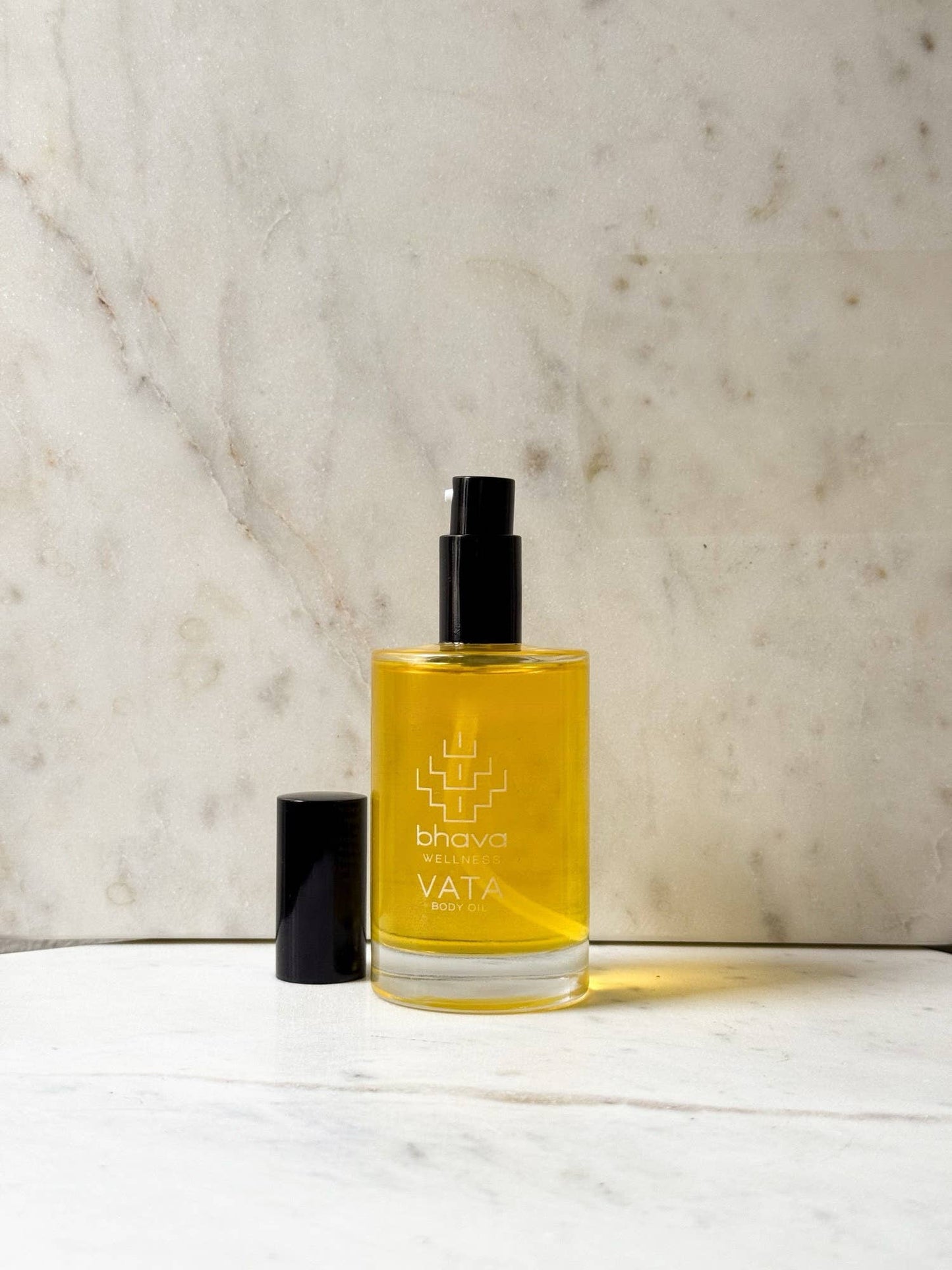 A bottle of bhava VATA Ayurvedic oil with a black spray cap, placed on a white marble surface against a beige marble background.