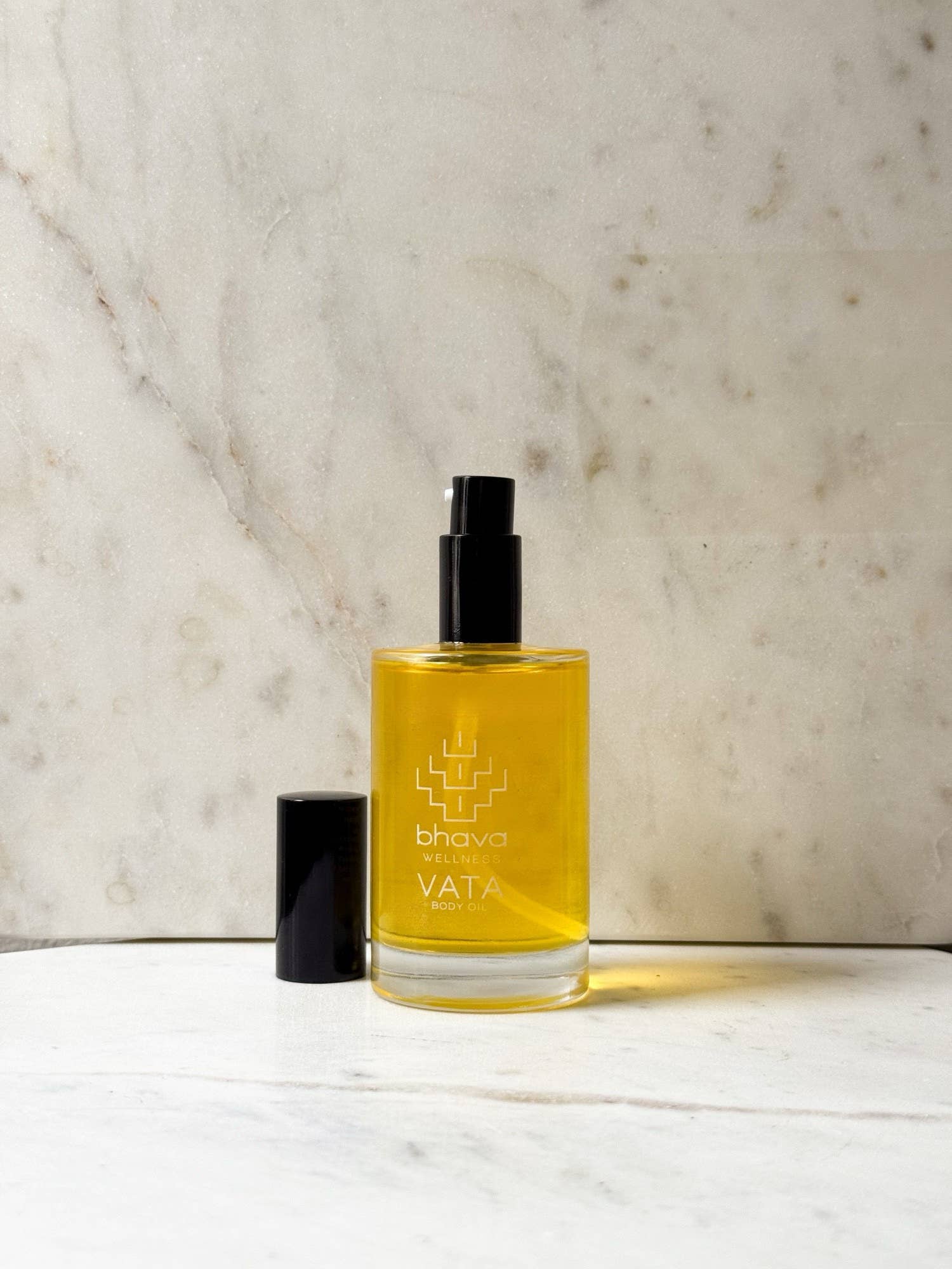A bottle of bhava VATA Ayurvedic oil with a black spray cap, placed on a white marble surface against a beige marble background.