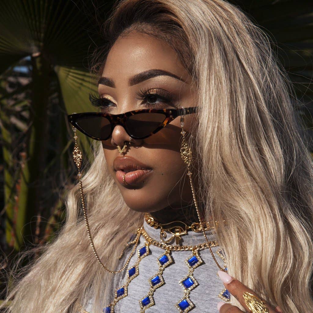 Woman wearing sunglasses and gold jewelry with a blurred natural background
