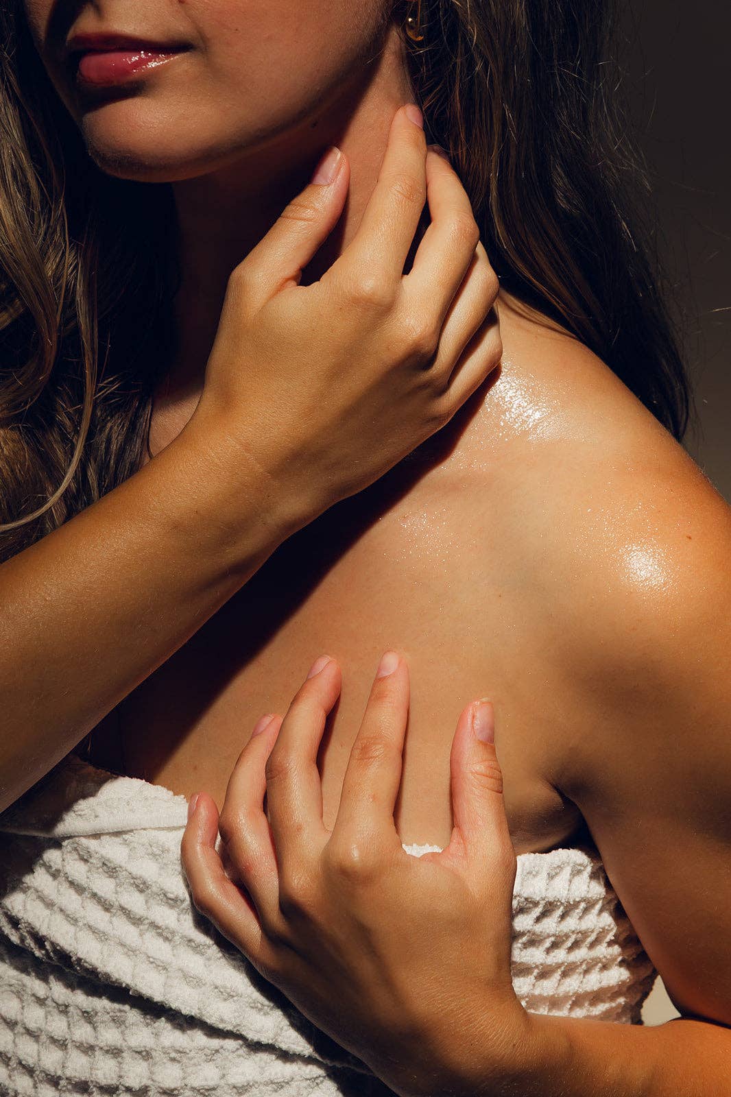 Close-up of a person with hands on their shoulders, wearing a textured white garment.