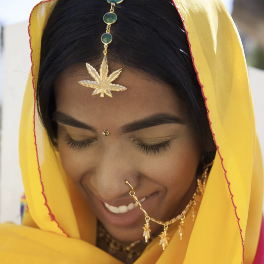 woman wearing a gold weed leaf head jewel down her center part 