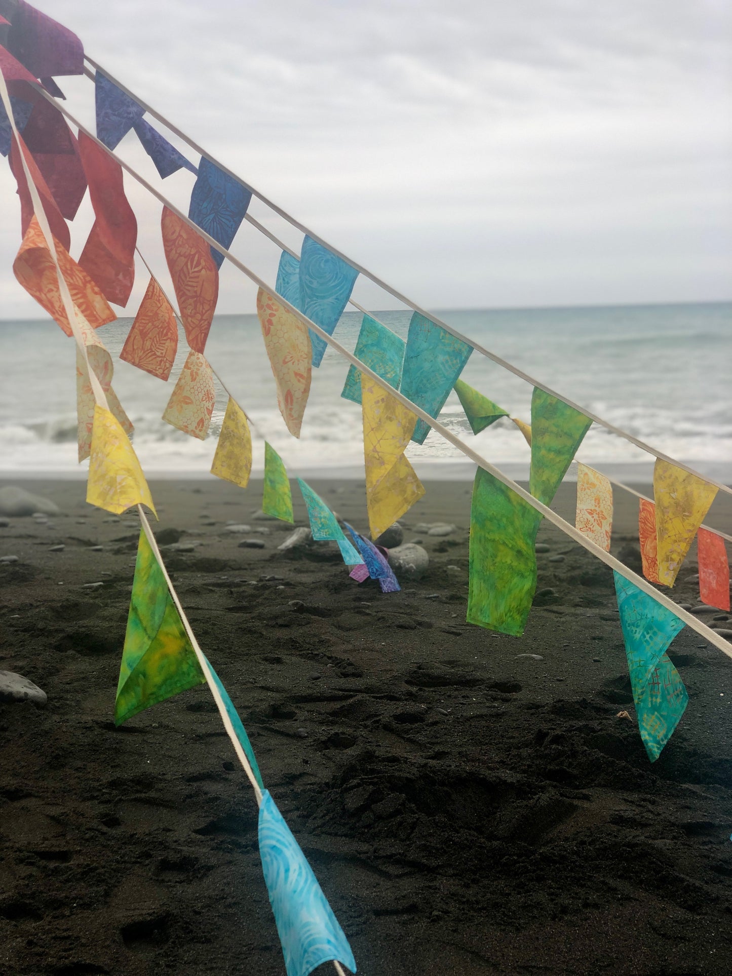 rainbow bunting flags are draped to create a tibetan prayer flag display on the beach