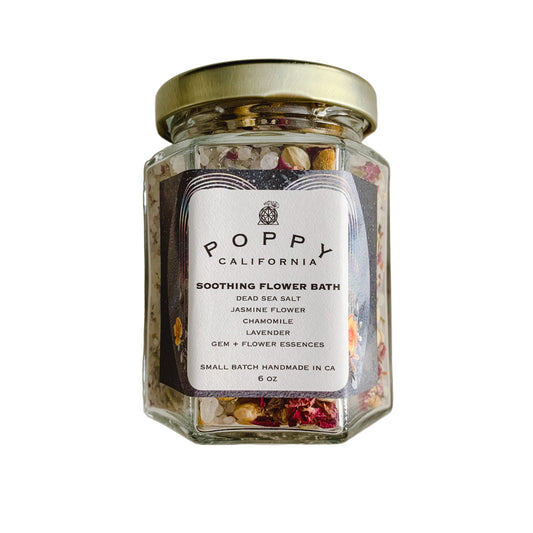 Glass jar of Poppy California soothing flower bath with a gold lid on a neutral background.