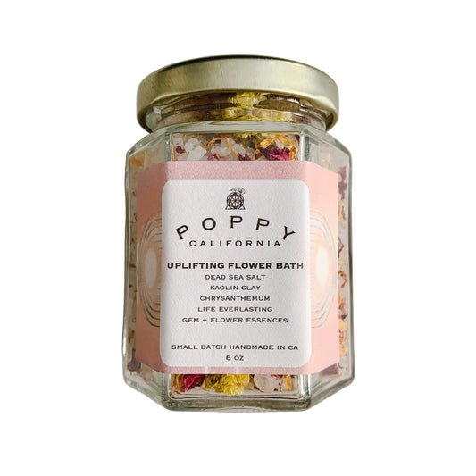 Glass jar of 'Uplifting Flower Bath' with a 'Poppy California' label on a neutral background.